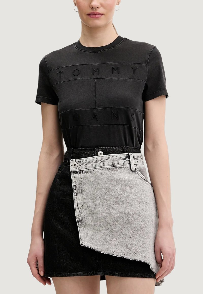 Schwarzes Baumwoll-T-Shirt mit erhabenen "TOMMY" und "JEANS" Schriftzügen. Kombiniert mit einem asymmetrisch geschnittenen schwarzen und grauen Jeansrock mit ausgefransten Kanten.