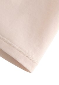 Bomulds T-shirt stof i en blød beige farve, med en glat tekstur og synlig pæn syning langs kanten for holdbarhed.