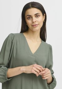 Blusa verde texturizzata con scollo a V, maniche a sbuffo e polsini arricciati, caratterizzata da motivi sottili e una vestibilità comoda.