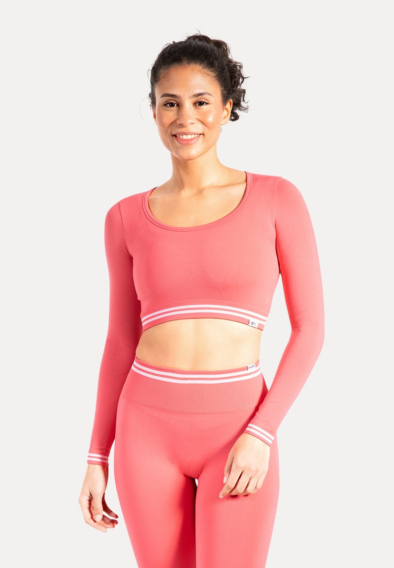 Crop top rosa a maniche lunghe con scollo rotondo e dettagli a righe bianche, abbinato a leggings coordinati a vita alta di colore simile.