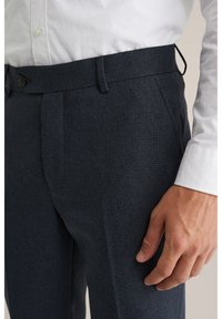 Laivastonsiniset, tekstuurilliset housut, joissa on hienovarainen ruutukuosi, sivutaskut ja suora etuosa. Kangas näyttää sileältä ja istuu hyvin vyötäröllä.