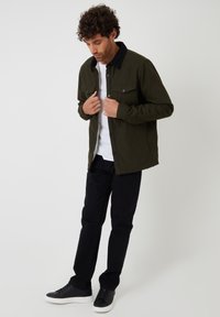 Jasnozielona kurtka z czarnym kołnierzem z kordurojowej tkaniny, dwiema przednimi kieszeniami i luźnym krojem. Połączona z czarnymi spodniami i czarnymi trampkami.