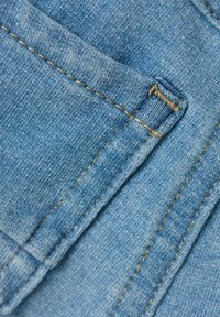 Detajlni pogled na svetlo modro jeans tkanino z zanko za pas in dvojno šivane šive v rjavi niti.