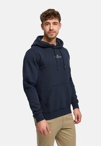 Laivastonsininen puuvillainen huppari kengurun taskulla, säädettävällä kiristysnauhalla hupussa ja pienellä merkin logolla rinnassa. Pehmeä pinta.