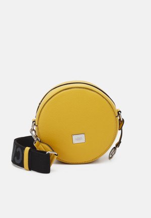 Ronde gele leren crossbodytas met zwarte verstelbare band en zilverkleurige hardware op witte achtergrond.