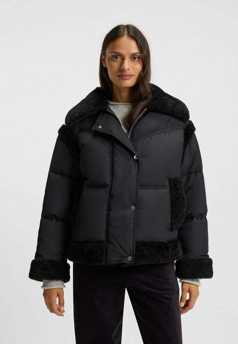 Giacca a vento nera con colletto e polsini in shearling nero strutturato, dotata di chiusura con zip, tasche laterali e silhouette ampia.