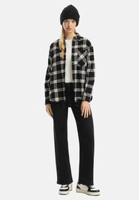 Zwart-wit geruite flanellen shirt met een losse pasvorm, zwarte beanie, wit T-shirt en zwarte wijde broek, gecombineerd met zwart-witte sneakers.