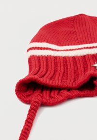 Czerwona, dzianinowa czapka z prążkowanej struktury, z białymi paskami i sznurkiem ściągającym. Zawiera dekoracyjny akcent w formie gwiazdki.