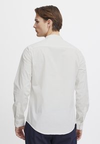Weißes Langarmhemd mit einem klassischen Kragen, Knopfmanschetten und einem glatten, leichten Stoff. Die Rückansicht zeigt eine taillierte Passform und eine Schulterpasse.