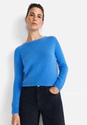 Maglione morbido blu lavorato a maglia con scollatura a barca e maniche lunghe, abbinato a jeans neri a vita alta. Il tessuto ha una consistenza pelosa.
