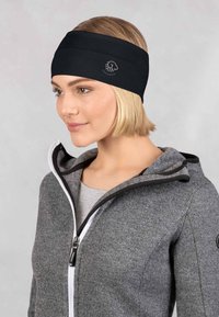 Zwarte hoofdband gemaakt van een gladde, rekbare stof. Heeft een logo aan de zijkant. Draagt een grijze zip-up jas.