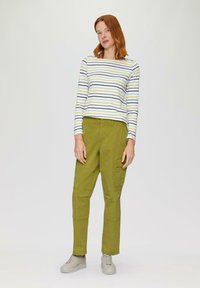 Langemouwen gestreepte shirt in wit, marineblauw en geel, gecombineerd met olijfgroene cargobroek. Lichtgrijze sneakers met gestructureerde zolen.
