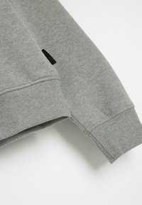 Szary sweatshirt z prążkowanymi mankietami i teksturowanym materiałem. Posiada małą czarną metkę na rękawie. Czysty i minimalistyczny design.