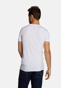 Witte T-shirt met korte mouwen en een ronde hals, met een gladde textuur, aansluitend ontwerp en een eenvoudige achterkant. Draagbaar met donkerblauwe jeans.