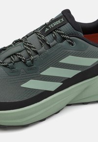 Pantof green pentru sport cu un superior din plasă texturată, dotat cu accente negre, trei dungi verde deschis și o talpă ondulată din cauciuc.