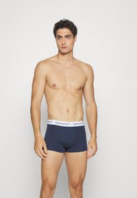 Dunkelblaue Baumwoll-Boxershorts mit einem weißen Bund, der das "GANT"-Logo zeigt. Fitted Design und glatte Textur.