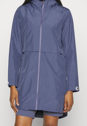 Kvinde iført en langærmet, hætteklædt, vandtæt lilla regnfrakke med lynlås foran og knapmanchetter.