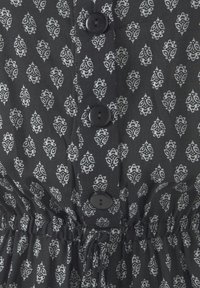 Černá látka s bílým složitým květinovým vzorem, s knoflíky a elastickým pásem pro tvar a padnutí. Měkká textura.