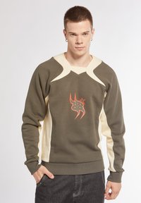 Felpa verde con dettagli beige, presenta un design a scollo a V, maniche lunghe e una grafica arancione sul davanti. Tessuto morbido.