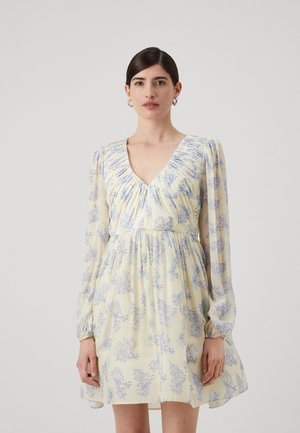 Kukullinen mekko vaaleankeltaisena sinisillä kuvioilla, jossa on V-pääntie, rypytetty yläosa ja läpikuultavat pitkät hihat.