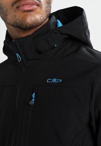 Black jacket with hood, featuring blue accents and zippers. It has a smooth texture and a logo on the chest. Functional design.