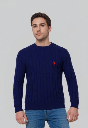 Navyblauwe kabelbreisweater met geribbelde manchetten en onderrand, voorzien van een klein rood logo op de borst. Gemaakt van een zachte, gestructureerde stof.