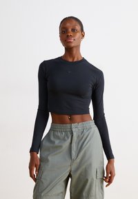 Fekete, rövidített, hosszú ujjú felső, sima anyagból, kerek nyakkal és diszkrét Nike logoval. Világoszöld cargo nadrággal párosítva.