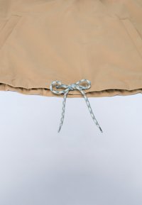 Beżowy brzeg ubrania z dwoma przednimi kieszeniami i niebiesko-białym sznurkiem zawiązanym na kokardę na środku dolnej krawędzi.