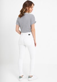 Calças de ganga brancas justas combinadas com uma blusa de manga curta às riscas preta e branca, com um decote redondo e mangas dobradas.