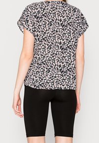Blouse fleurie à manches courtes, avec un fond noir orné de petites fleurs blanches et roses ; portée avec un short noir ajusté.