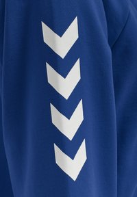 Blåt stof med en lodret række af fire hvide chevronpile, der peger nedad, trykt på overfladen.