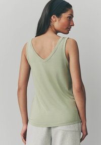 Top sin mangas de color verde claro con un diseño de escote en V, hecho de un tejido suave, combinado con pantalones de chándal grises. Vista trasera, textura suave.