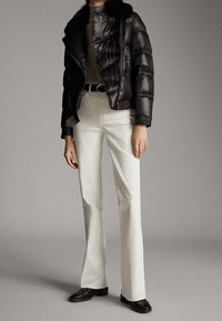 Zwarte pufferjas met een bontkraag, beige coltrui, witte flared broek en zwarte leren schoenen, met een getailleerde pasvorm.