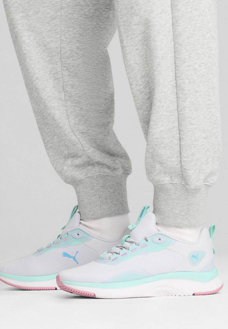 Scarpe atletiche leggere in bianco e azzurro chiaro, con una parte superiore in rete liscia, suola rosa e elementi di design minimalisti.
