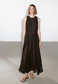 Black, sleeveless maxi dress with a loose fit, featuring a textured fabric and uneven hem. Worn with red flip-flops. Simple, elegant design.