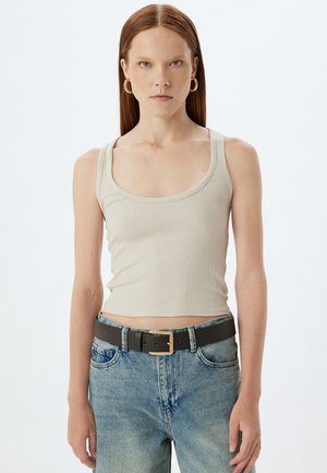 Débardeur beige à côtes avec de larges bretelles, associé à un jean en denim bleu clair et une ceinture noire avec une boucle dorée.