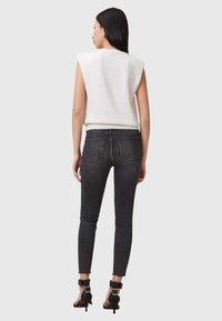 Top blanco sin mangas con hombreras, combinado con jeans ajustados gris oscuro y tacones negros con tiras y detalle de hebilla en el tobillo.