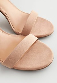 Nude mockasinsandaler i suède med ett brett band över foten, öppen tå och en slät innersula. Platt, rundad sula med en lätt kurva.