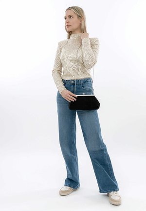 Zwarte corduroy clutch tas met zilveren hardware, gedragen met een beige tops met pailletten en blauwe high-waisted jeans. Chunky witte sneakers maken de look compleet.