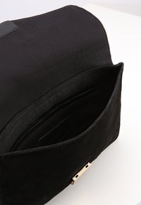 Svart mockaväsk med magnetisk klaffstängning. Inuti finns flera kortfack och en mjuk foder. Minimalistisk design.