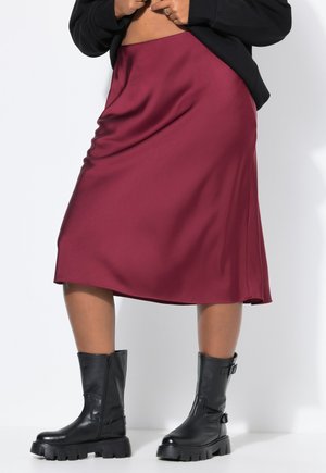Bordeauxfarbene Satin-Midirock mit glatter Textur, der ein fließendes Design und eine dezente A-Linie aufweist. Kombiniert mit robusten schwarzen Lederstiefeln.