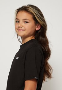 Svart bomull T-shirt med en liten vit "VANS"-logotyp på bröstet och ärmen. Designen inkluderar rund halsringning och korta ärmar.