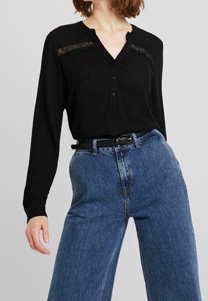 Zwarte lange mouw shirt met kanten accenten, V-hals en knoopsluiting, gecombineerd met een losse, hoge taille blauwe jeans.