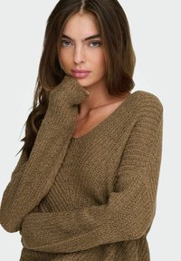 Maglione marrone lavorato a maglia con scollo a V, tessuto testurizzato e maniche lunghe. Presenta una vestibilità ampia e polsini a coste per un tocco in più.