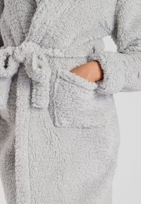 Robe léger gris clair, moelleux, en matériau texturé et en peluche. Doté d'une taille à nouer et de poches avant, mettant en valeur un design doux et confortable.