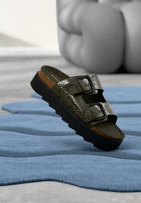 Πράσινο σανδάλι slide με τύπωμα φίδι, δύο μαύρες λουρίδες με αγκράφες, πάτο από φελλό, παχύ μαύρο πέλμα και υφή στην πάνω επιφάνεια.