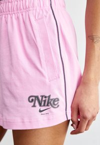 Růžové bavlněné šortky s elastickým pasem, bočními kapsami a šedým lemem, s výrazným logem Nike a nápisem "Od roku 1972."