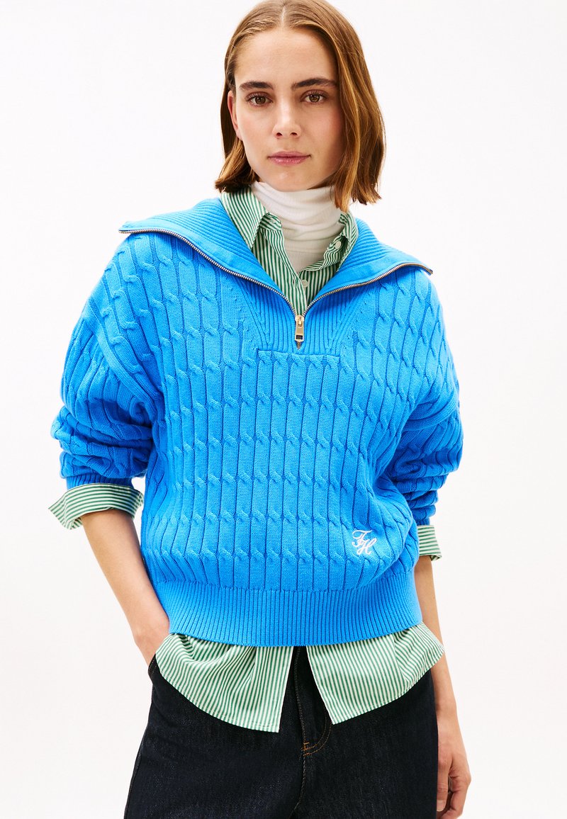 Pulover albastru tricotat, cu guler cu fermoar, având un model texturat cu dungi.