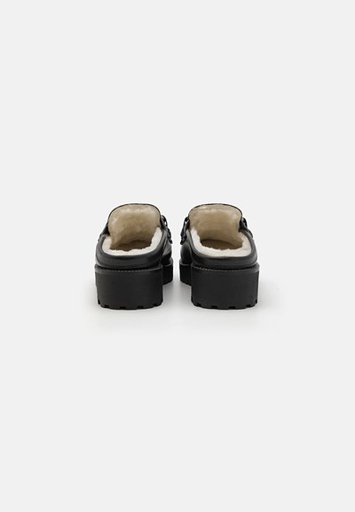 Black clogs with a chunky sole, featuring a soft, cream-colored faux fur lining. Minimalist design with no visible hardware.