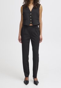 Black tailored vest with a V-neckline and four gold buttons, paired with fitted black pants featuring a flat waistband and front pleats.